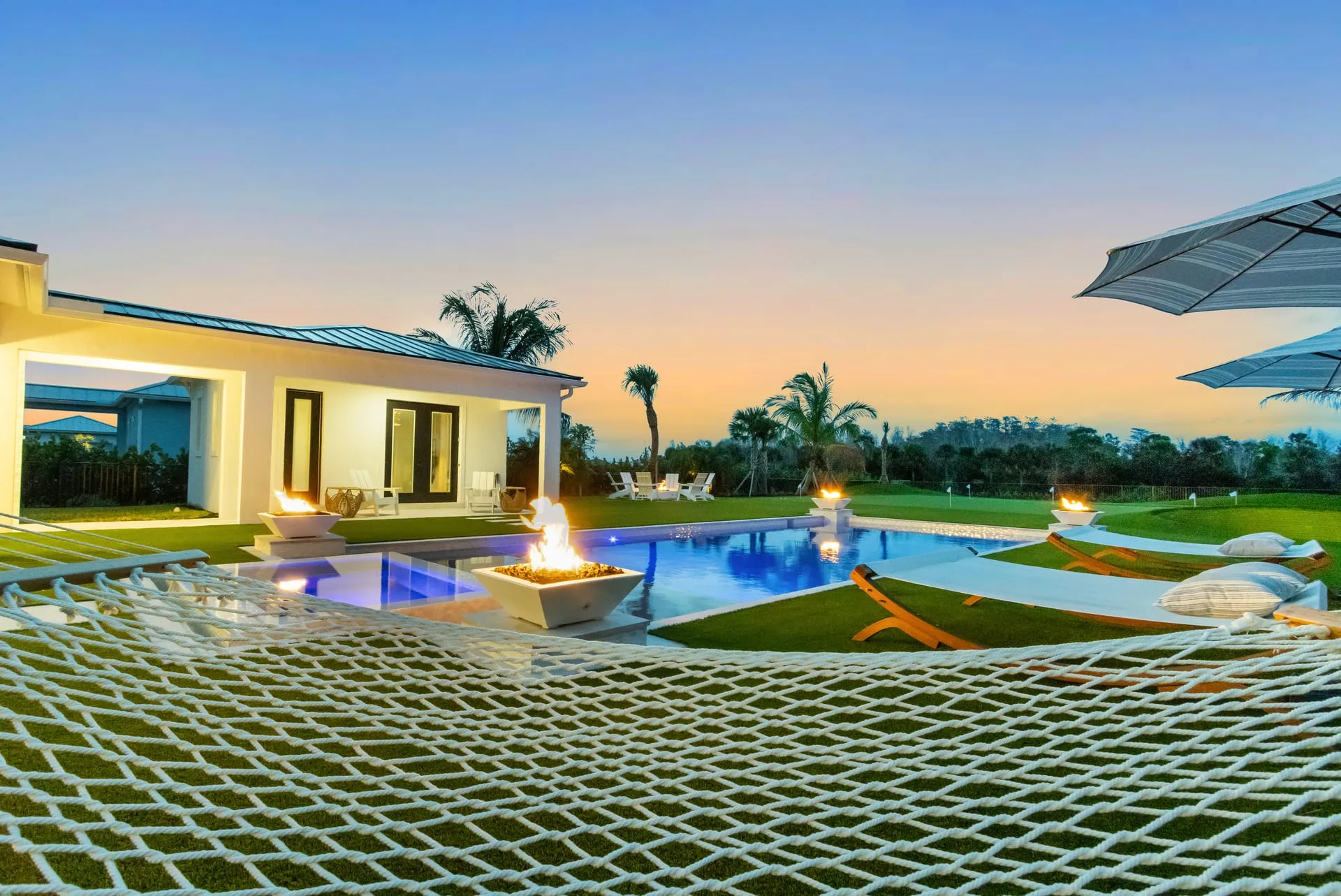 Twilight pool seen from a net-hammock deck, with fire bowls glowing beside the water