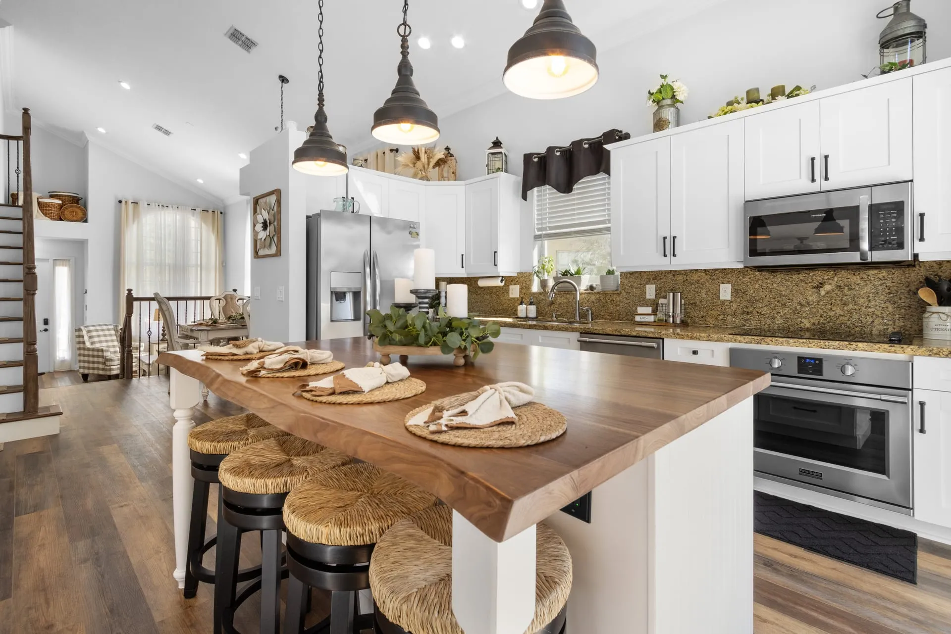 White kitchen with a live-edge wood island, rattan counter stools and pendant lights