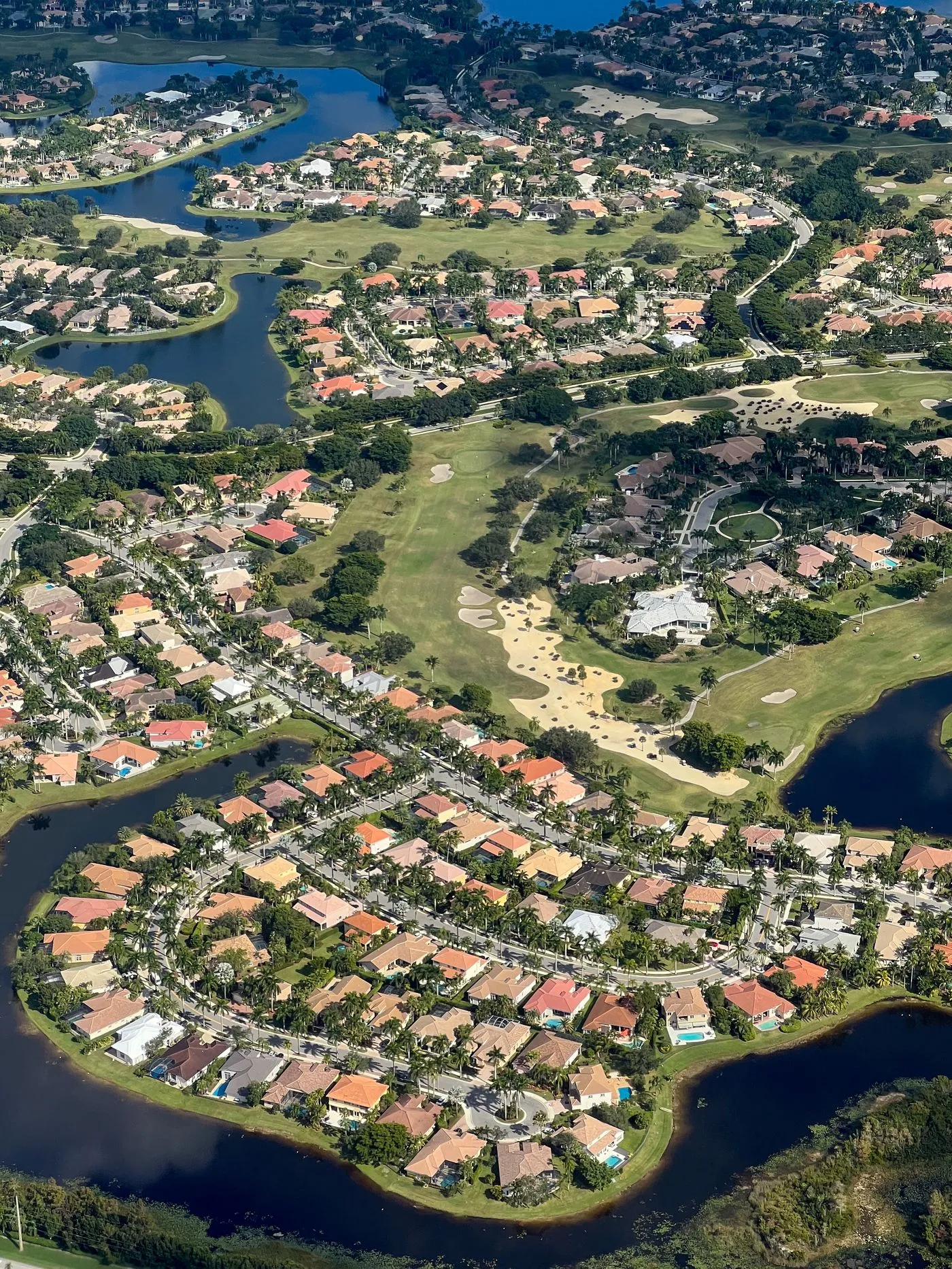 Drone aerial photography of a 55+ golf course community with tile-roof homes, palms and lakes near The Villages FL