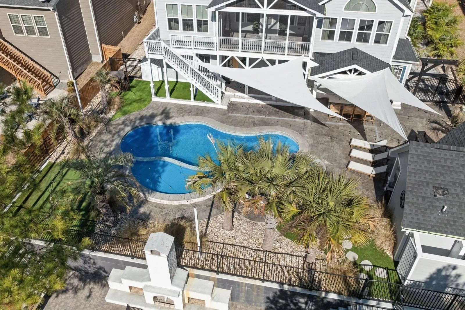 Aerial view of a fenced backyard with a freeform pool, palms and a covered porch
